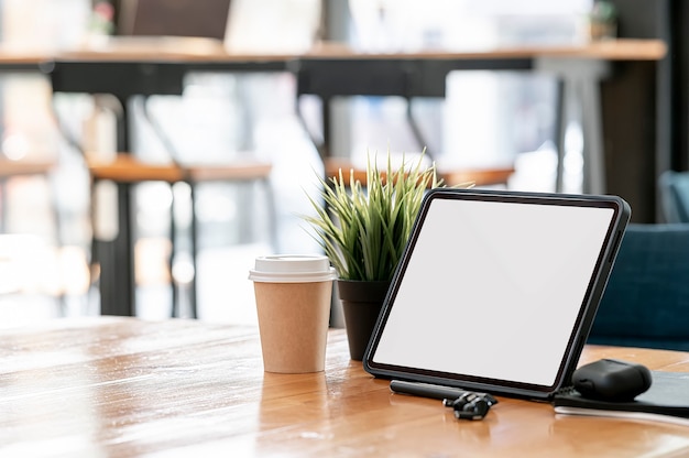 Area di lavoro con tablet schermo vuoto e gadget su tavolo in legno in co-workspace.