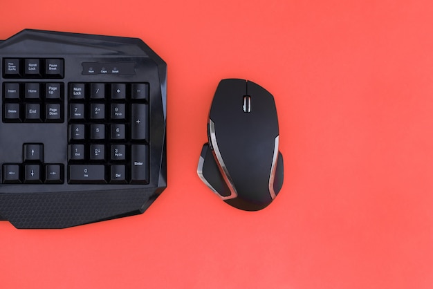 Area di lavoro con tastiera e mouse su uno sfondo rosso. Copyspace. Mouse nero, tastiera isolata