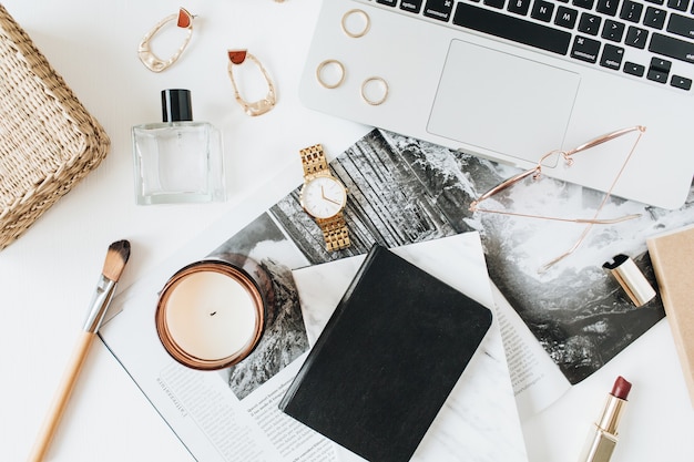 Area di lavoro femminile moderna home office scrivania con accessori per la spazzola del rossetto dell'orologio del profumo del computer portatile su superficie bianca vista dall'alto piatto laici Concetto di capo della ragazza