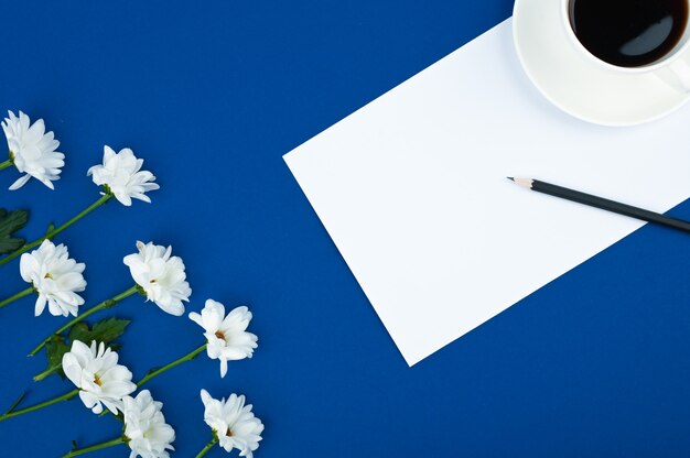 Area di lavoro femminile. Una tazza di caffè e cornice di fiori su spazio blu. Copia spazio