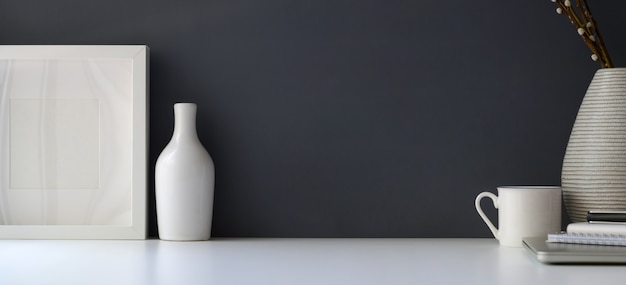 Area di lavoro moderna con cornice vuota e vaso in ceramica sul tavolo bianco e sfondo grigio muro