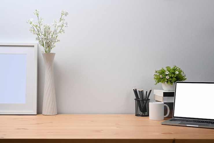 Foto area di lavoro moderna con laptop, tazza di caffè, portamatite, libri e pianta d'appartamento su tavolo di legno.