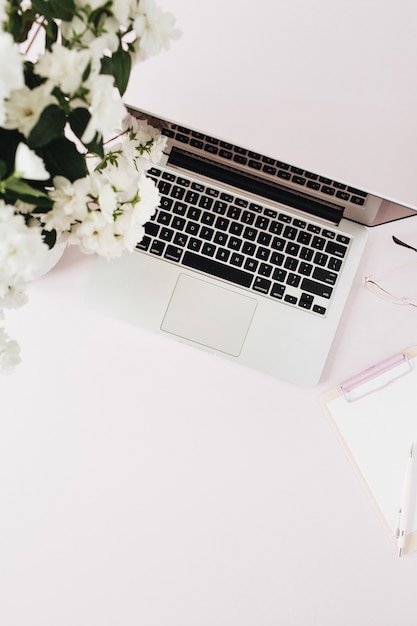 Area di lavoro scrivania da ufficio con laptop, bouquet di fiori e appunti sul tavolo rosa