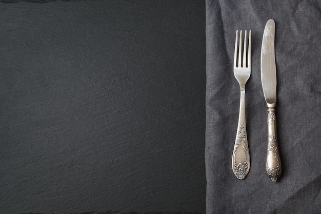 Argenteria rustica in tovagliolo di lino grigio e piatto in ardesia nera con spazio per la copia Vista dall'alto