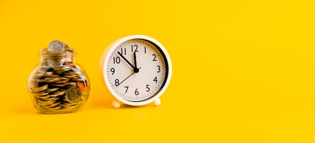 Argento in una bottiglia di vetro e un orologio bianco su sfondo giallo concetto di risparmio e tempo da vivere