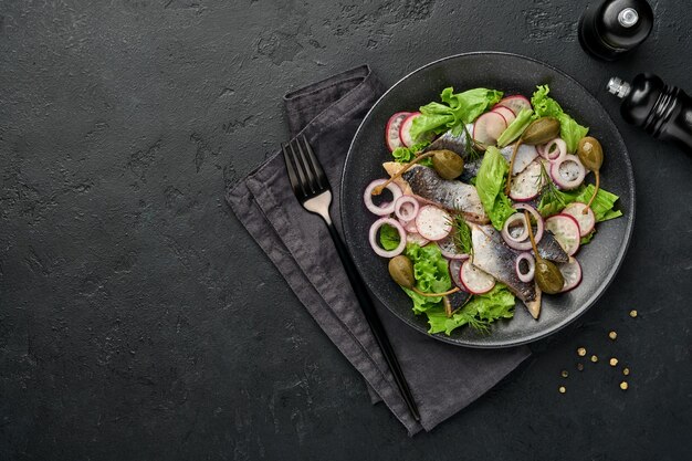 aringa salata con spezie, capperi, erbe aromatiche e insalata di cipolle su piastra nera su sfondo scuro