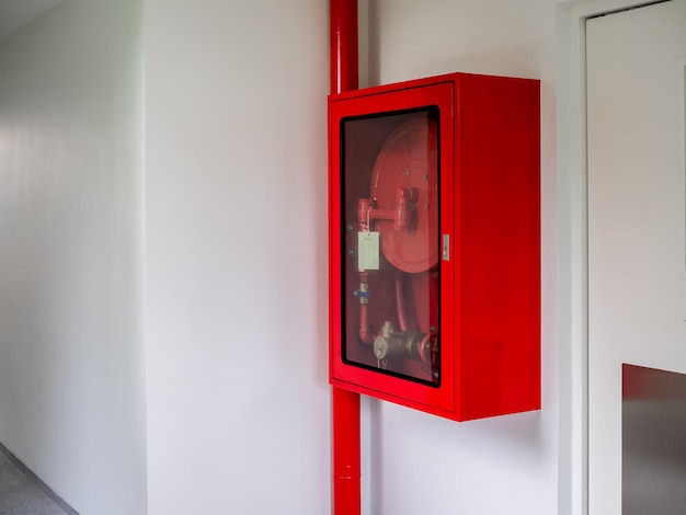 Armadietto per estintori montato sulla parete nell'angolo dell'edificio bianco dell'hotel Cassetta di emergenza rossa chiusa con estintore e attrezzatura di sicurezza con avvolgitubo antincendio per prevenire gli incendi