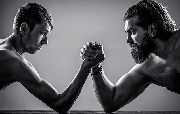 Arms wrestling mano sottile grande braccio forte in studio Uomo barbuto molto muscoloso braccio di ferro un uomo debole e gracile