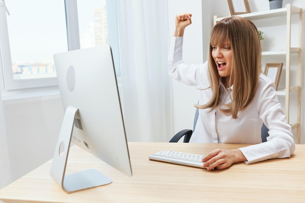 Arrabbiata donna d'affari bionda malvagia che urla al desktop agitando il pugno sullo schermo seduto sul posto di lavoro in un ufficio moderno Il regista irritato lavora sul computer online nella società finanziaria Copia spazio