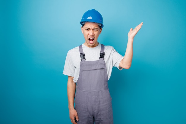 Arrabbiato giovane operaio edile indossando il casco di sicurezza e uniforme che mostra la mano vuota