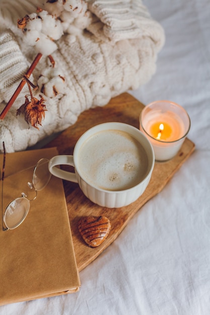 Arredamento accogliente per la casa. Una tazza di cappuccino, biscotti, una candela sul letto. Mattina d'inverno. Autunno.