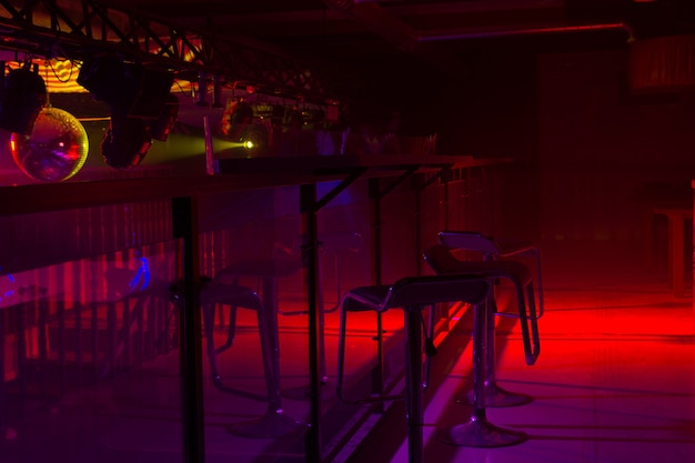 Arredamento moderno del bar e illuminazione stroboscopica colorata rossa e viola che illumina una fila di eleganti sgabelli da bar a un bancone
