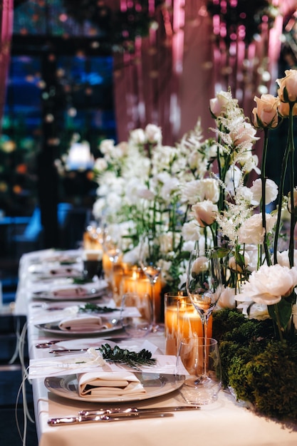 Arredamento romantico del piano del tavolo da matrimonio con grandi mazzi floreali lussureggianti tra cui rose bianche ranun...