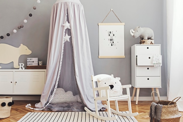 Arredamento scandinavo elegante e luminoso della stanza del neonato con poster, mobili di design bianchi, giocattoli naturali, baldacchino grigio sospeso con culla in legno, leggio e accessori