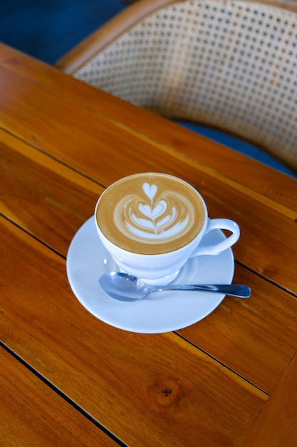 Arte del latte su cappuccino in tazza bianca al tavolo di caffè in legno