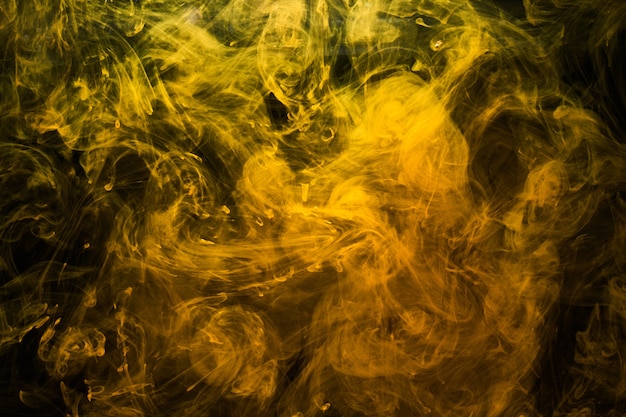 Arte liquida astratta, fumogeno giallo su sfondo nero, colori acrilici color ambra sott'acqua