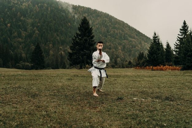 Arte marziale del karate un uomo in kimono con cintura nera si allena sullo spazio libero della montagna