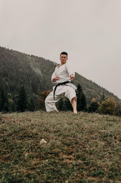 Arte marziale del karate un uomo in kimono con cintura nera si allena sullo spazio libero della montagna