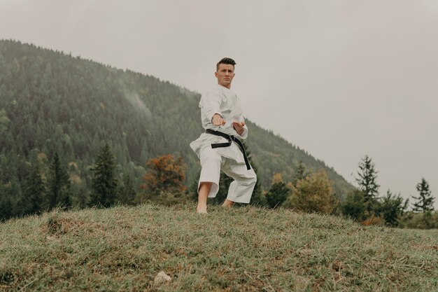 Arte marziale del karate un uomo in kimono con cintura nera si allena sullo spazio libero della montagna