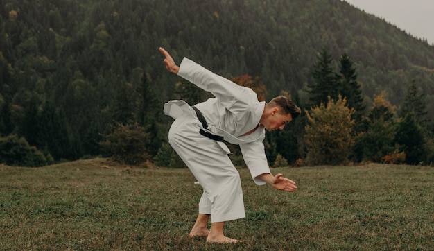 Arte marziale del karate un uomo in kimono con cintura nera si allena sullo spazio libero della montagna