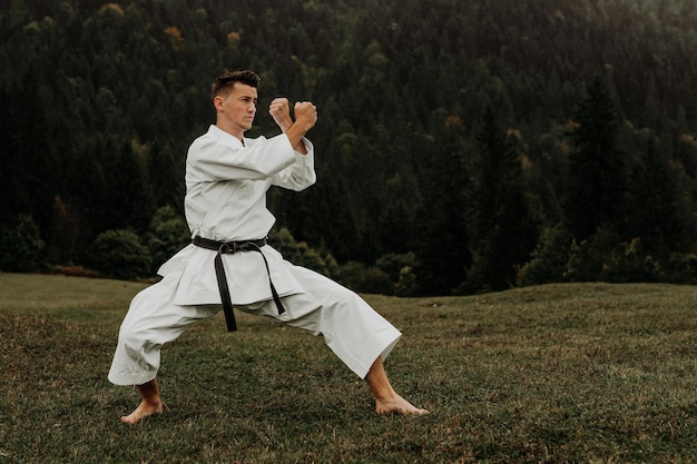 Arte marziale del karate un uomo in kimono con cintura nera si allena sullo spazio libero della montagna