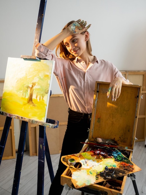 Arte visiva Artista pittore Hobby creativo Stanco rilassato donna sorridente con le mani sporche giallo natura astratta opera d'arte su cavalletto tavolozza di vernice forniture in studio di casa leggero