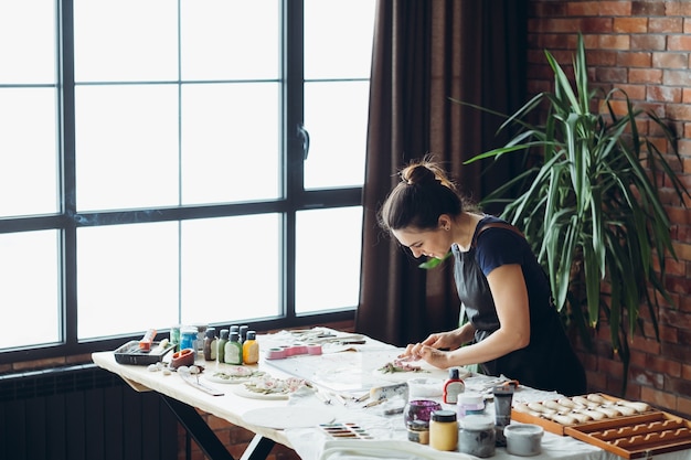 Artigianato in ceramica. Opera in lavorazione. Ispirazione alla luce del giorno del mattino. Giovane donna con strumenti di modellazione