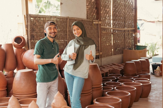 Artigiano a donna velata con i pollici in su in piedi tra le ceramiche