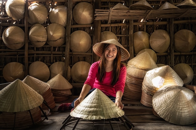 Artigiano femminile del viaggiatore asiatico che fa il cappello tradizionale del Vietnam nel vecchio tradizionale