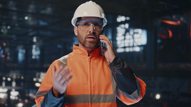 Artigiano professionista che parla al cellulare nel magazzino della fabbrica in uniforme da vicino