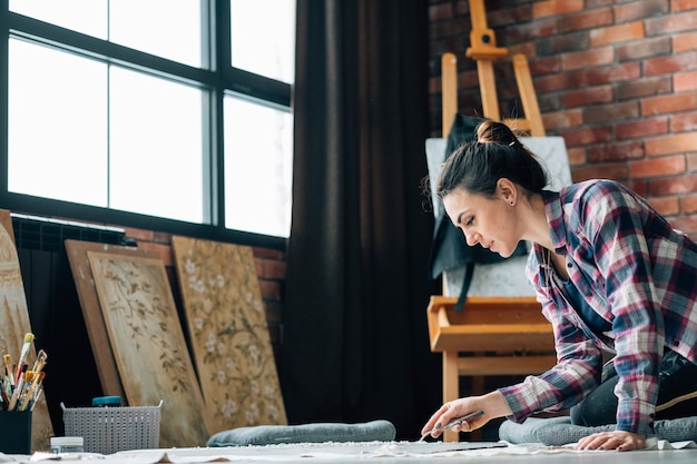 Artista al lavoro. Atmosfera creativa. Abitudini di vita. Donna con dipinto sul pavimento. Opere d'arte e forniture d'arte in giro.