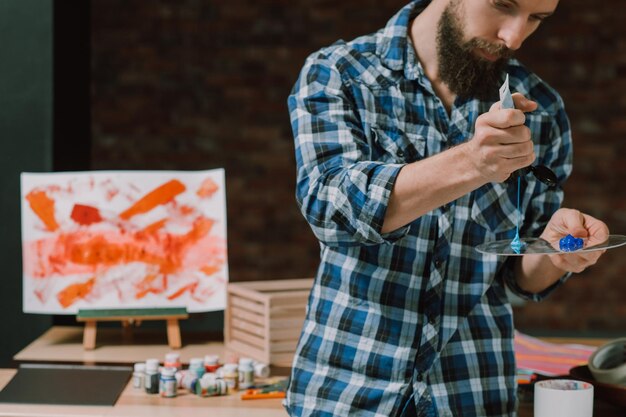 Artista al lavoro Giovane uomo barbuto dipinge sulla tavolozza Espressione facciale seria Concentrarsi sull'idea creativa Opera d'arte in corso