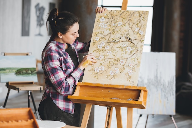 Artista al lavoro. Spazio di lavoro dello studio. Opera in lavorazione. Pittrice con strumento d'arte. Tela su cavalletto.