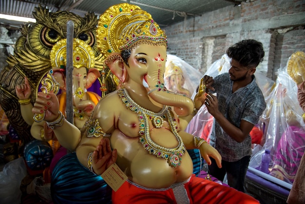 Artista che fa una statua e dà il tocco finale a un idolo del dio indù Lord Ganesha in un laboratorio di artisti per il festival di Ganesha