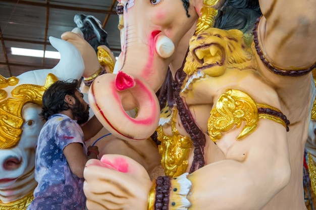 Artista che fa una statua e dà il tocco finale a un idolo del dio indù Lord Ganesha in un laboratorio di artisti per il festival di Ganesha