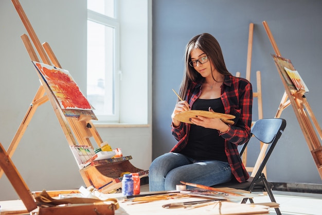 artista che tiene in mano un pennello e disegna un quadro su tela