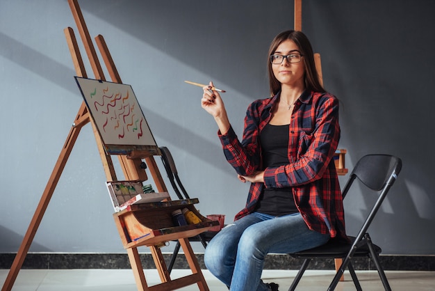 Artista dai capelli scuri che tiene in mano un pennello e disegna un quadro su tela.