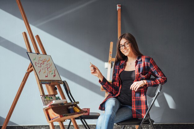 Artista dai capelli scuri che tiene in mano un pennello e disegna un quadro su tela.