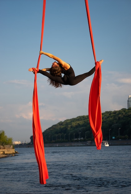 Artista di circo femminile bello e flessibile che balla con seta aerea con costa del cielo e del fiume