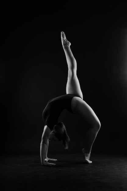 Artista di ginnastica ritmica ragazza flessibile che salta su sfondo bianco scuro grazia in azione di movimento