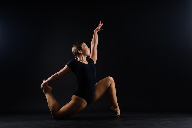 Artista di ginnastica ritmica ragazza flessibile che salta su sfondo bianco scuro grazia in azione di movimento