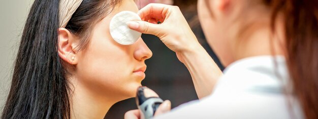 Artista di trucco che fa trucco professionale sul volto di una giovane donna usando un aerografo.