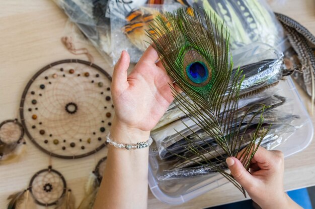 Artista femminile che sceglie piuma di pavone naturale per creare acchiappasogni all'amuleto dell'arredamento dell'officina