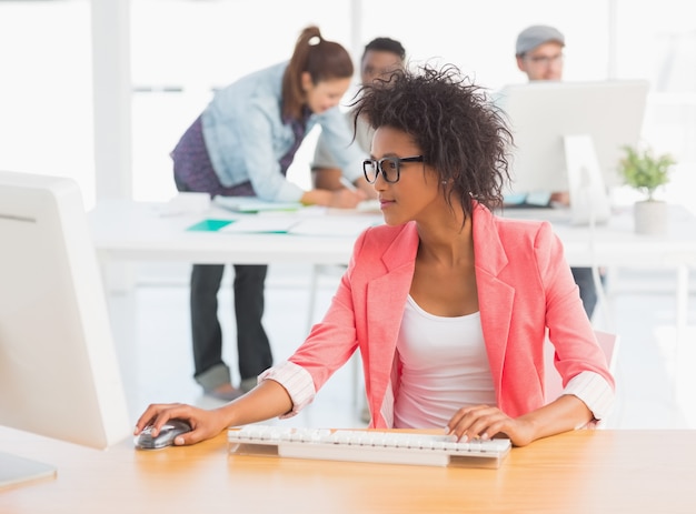 Artista femminile che utilizza computer con i colleghi nella priorità bassa all&#39;ufficio