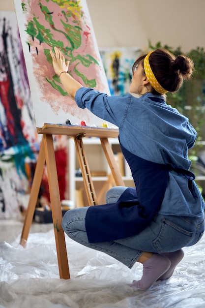 Artista femminile donna creativa in grembiule che crea il suo laboratorio di pittura astratta a casa studio