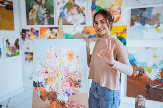 Artista femminile in piedi accanto al suo dipinto e mostrando il pollice in su