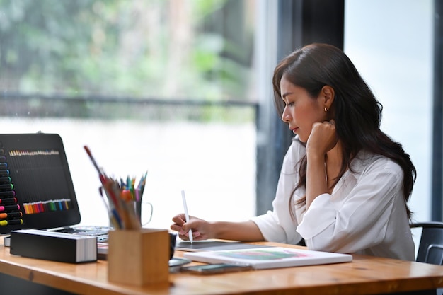 Artista femminile pacifica che lavora con la tavoletta digitale sul posto di lavoro moderno