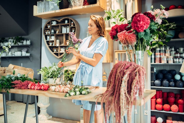 Artista floreale femminile ordina fiori freschi sul tavolo in negozio. Fiorista che fa bouquet sul posto di lavoro in boutique