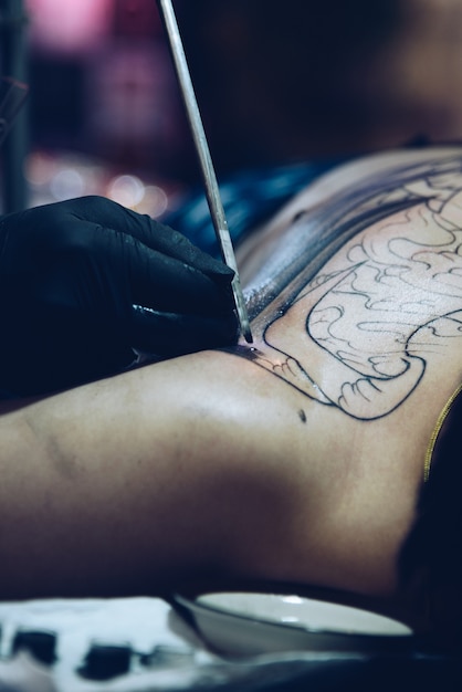 Artista professionista del tatuaggio che disegna arte sul corpo al negozio di tatuaggi