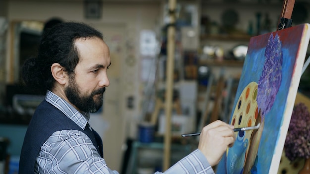Artista uomo concentrato che dipinge foto di natura morta su tela in studio d'arte al chiuso